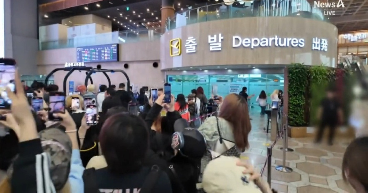 공항 출발 게이트 앞에 많은 사람들이 스마트폰으로 사진을 찍고 있는 모습