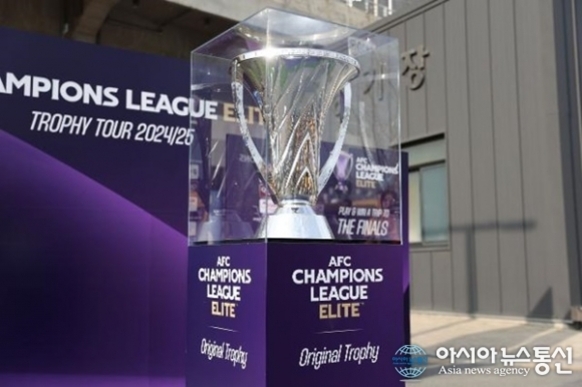 투명 케이스에 전시된 AFC 챔피언스 리그 엘리트 트로피가 보라색 받침대 위에 놓여 있다. 배경에는 'CHAMPIONS LEAGUE ELITE'와 'TROPHY TOUR 2024/25' 문구가 적혀 있다.