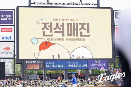 야구장 전광판에 '전석매진'이라는 문구와 캐릭터 이미지가 표시되어 있고, 관중들이 야구 경기를 관람하고 있다.