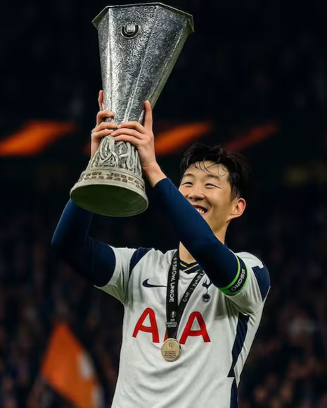 축구 유니폼을 입은 선수가 트로피를 들어올리며 환하게 웃고 있다.