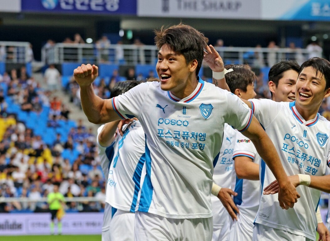 축구 경기장에서 흰색 유니폼을 입은 선수들이 골을 넣고 기뻐하며 함께 환호하고 있다.
