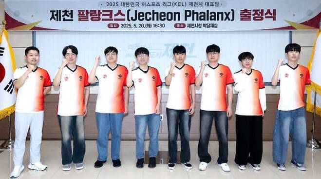 여덟 명의 남성이 제천 팔랑크스(Jecheon Phalanx) 출정식 행사에서 유니폼을 입고 단체 사진을 찍으며 주먹을 들어 올리고 있다. 배경에는 행사 현수막과 태극기가 보인다.