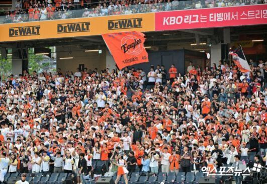 야구장 관중석에 많은 사람들이 모여 있고, 한화 이글스 깃발을 흔들며 응원하는 모습