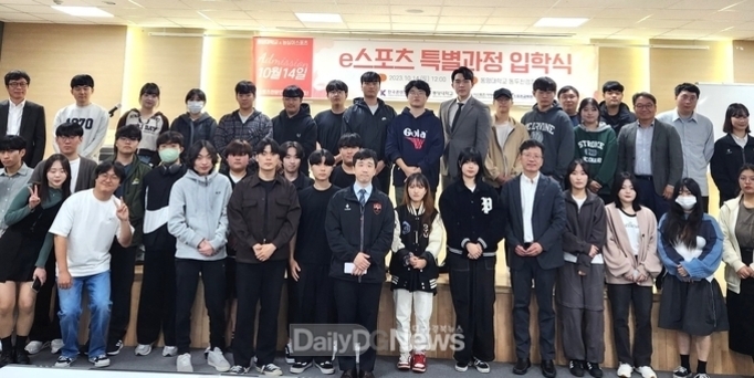 여러 명의 학생과 교직원들이 강당에서 'e스포츠 특별과정 입학식' 현수막 앞에 모여 단체사진을 찍고 있다.