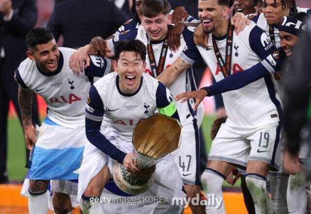 축구 경기 후 토트넘 홋스퍼 선수들이 우승 트로피를 들고 환하게 웃으며 기뻐하고 있다.