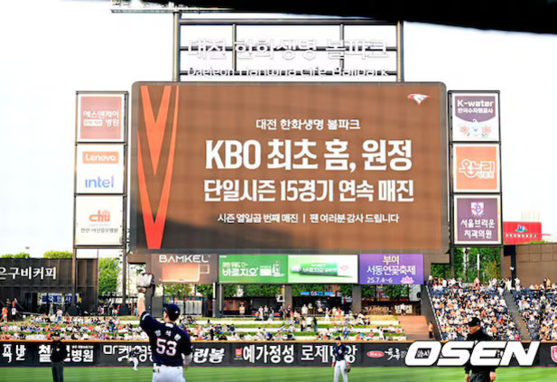 야구 경기장에서 대형 전광판에 'KBO 최초 홈, 원정 단일시즌 15경기 연속 매진'이라는 문구가 표시되어 있고, 관중들과 야구선수가 보인다.
