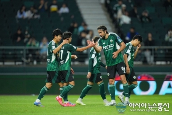 축구 경기장에서 초록색 유니폼을 입은 선수들이 하이파이브를 하며 기뻐하고 있다.