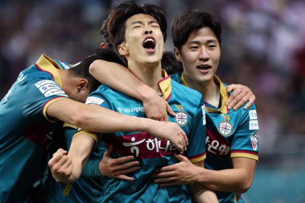 축구 경기에서 골을 넣고 환호하는 선수들이 서로를 끌어안고 기뻐하고 있다.