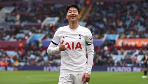 축구 경기장에서 흰색 유니폼을 입은 축구 선수가 엄지손가락을 치켜들고 미소 짓고 있다.