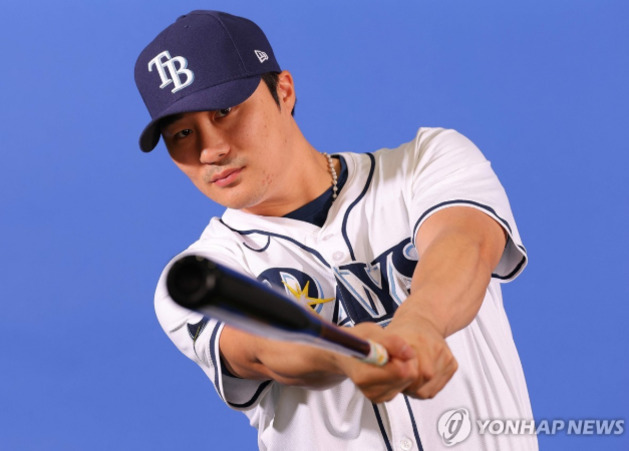 야구 유니폼과 모자를 착용한 남성이 배트를 들고 포즈를 취하고 있다.