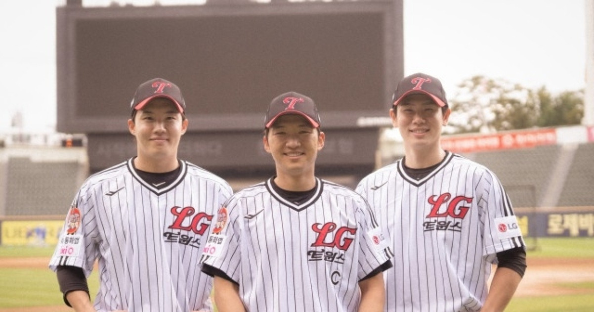 야구장에서 LG 트윈스 유니폼을 입은 세 명의 남성 야구선수가 나란히 서서 미소 짓고 있다.