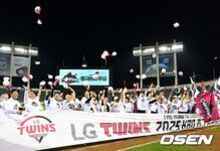 야구장에서 LG 트윈스 팀이 우승을 축하하며 모자를 던지고 기념 현수막을 들고 있는 모습