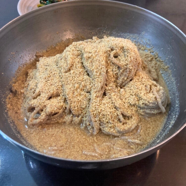 커다란 금속 그릇에 담긴 메밀국수 위에 진한 들깨가루와 국물이 듬뿍 뿌려져 있는 들깨국수