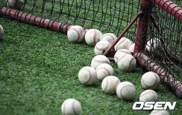 야구공 여러 개가 인조잔디 위에 흩어져 있고, 야구 네트가 보인다.