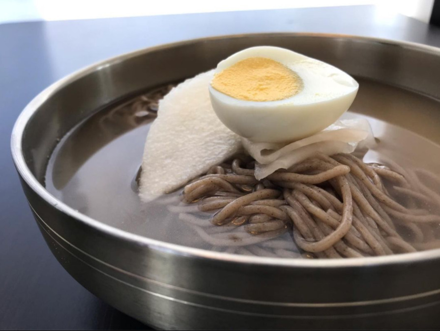 스테인리스 그릇에 담긴 냉면 위에 삶은 달걀 반쪽과 무절임이 올려져 있다.